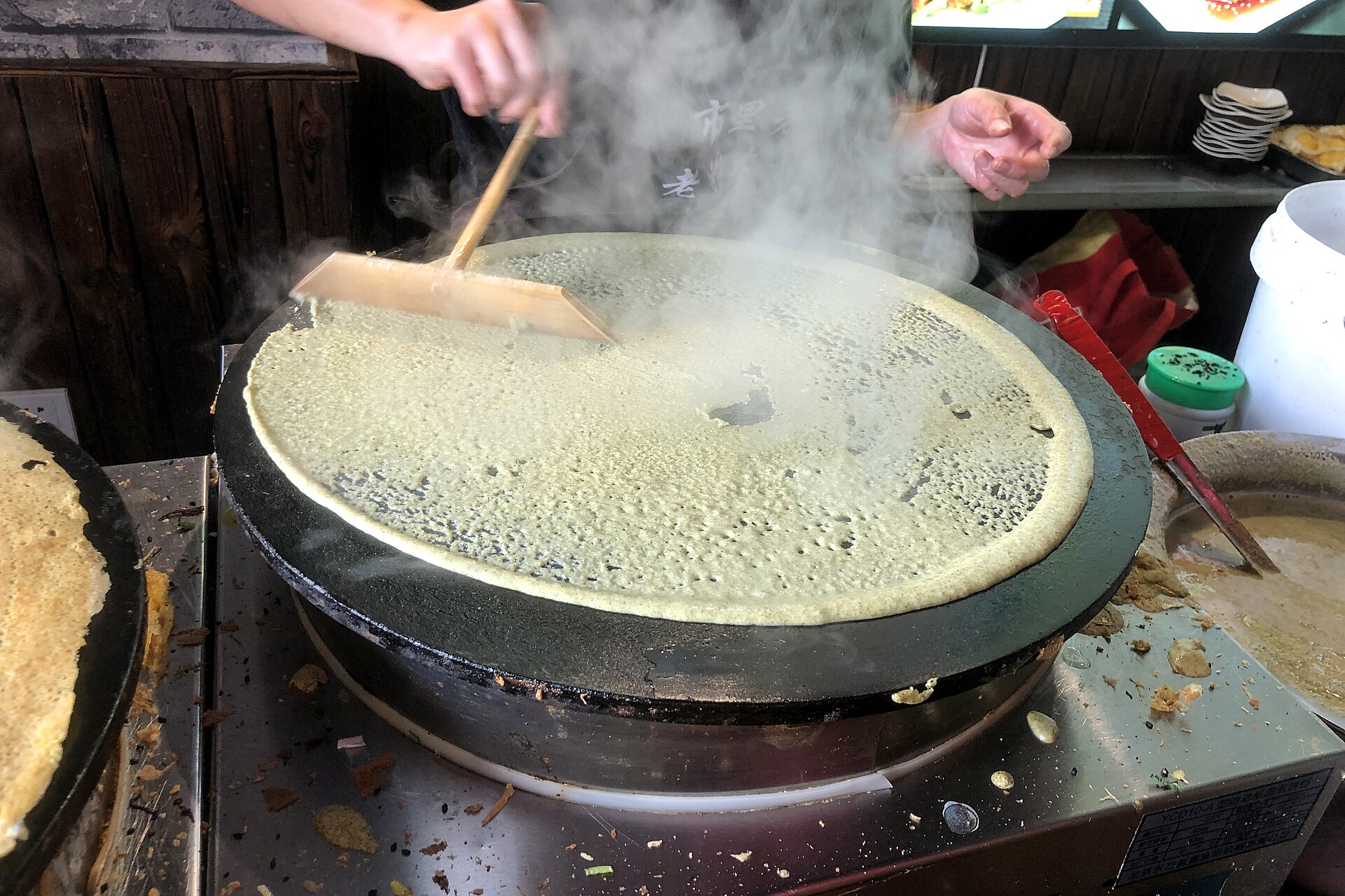 A vendor spreading jianbing batter across a hot round griddle in Binhai, Tianjin, in October 2019.