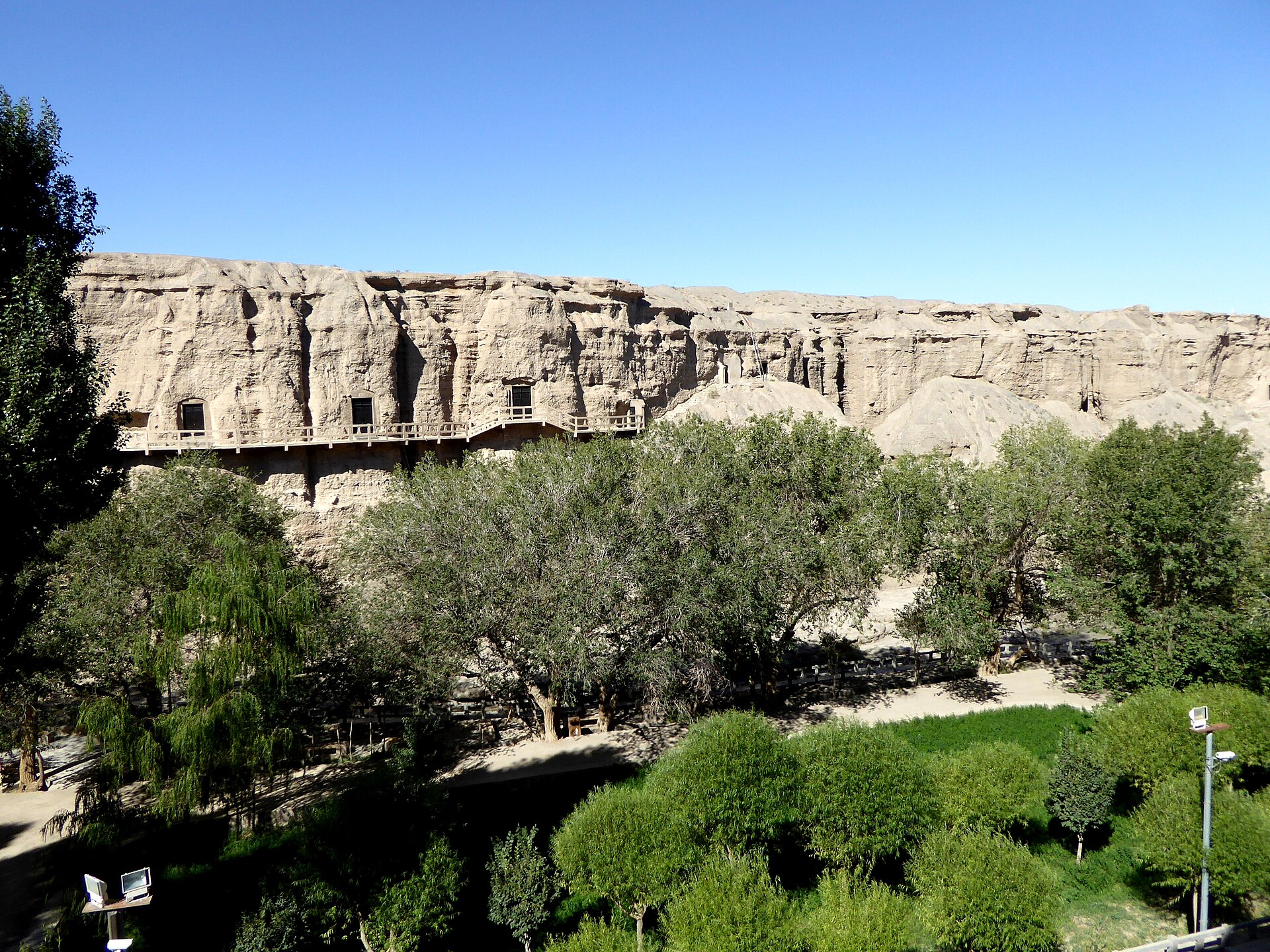 Cave openings and a raised walkway line the cliff at Yulin Caves in Gansu.