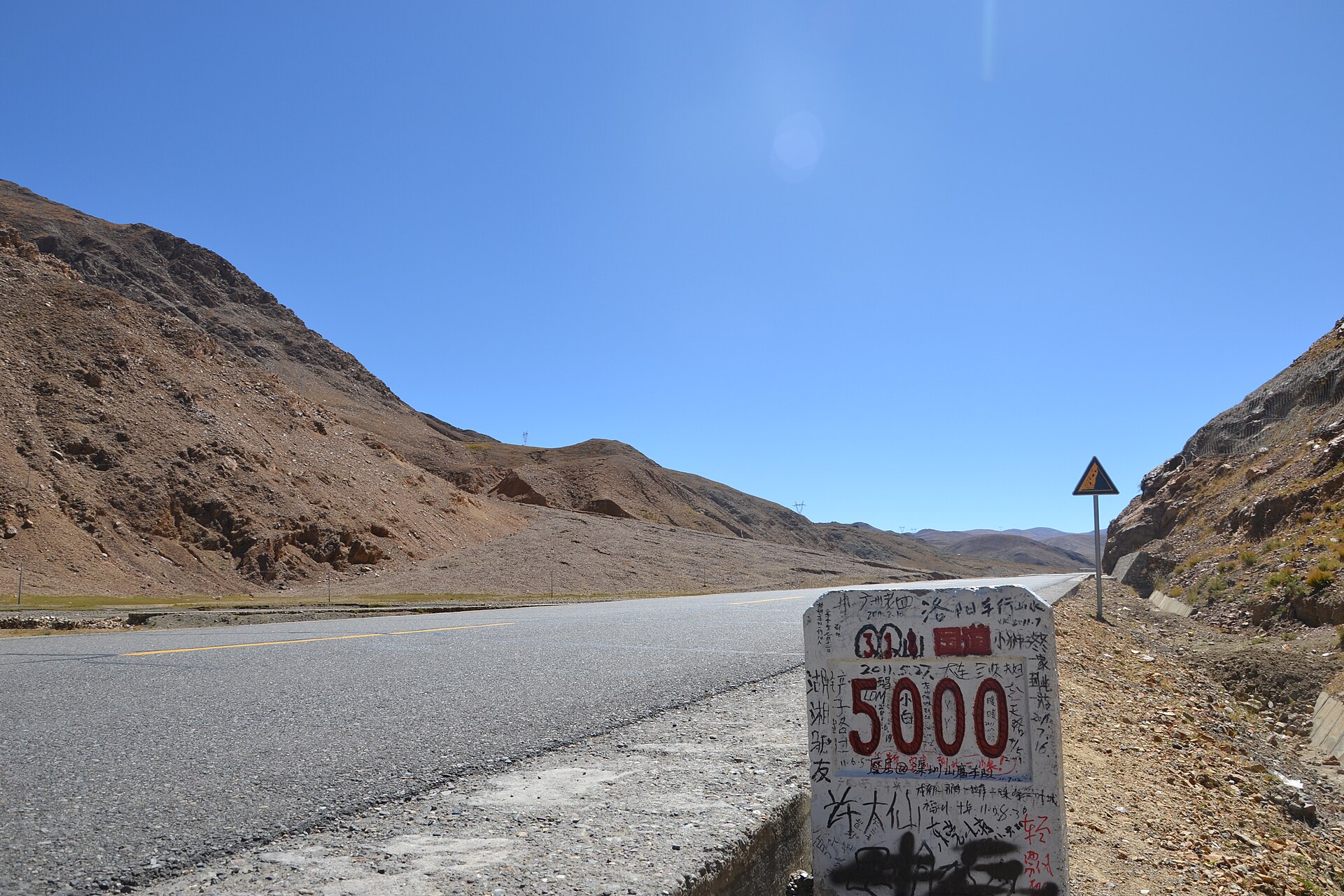 A G318 five-thousand-kilometre marker stands beside a mountain road in Lhatse County, Tibet.