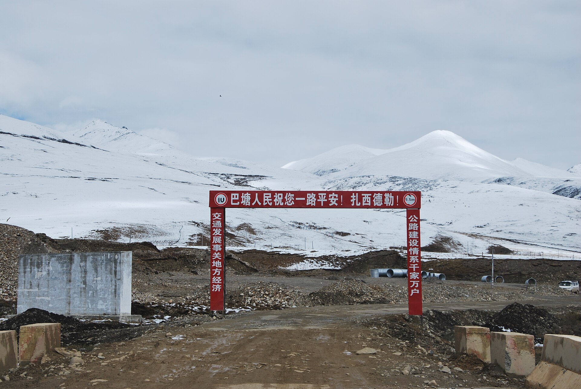 A road-works arch crosses G318 below snow-covered mountains in Batang County, Sichuan.