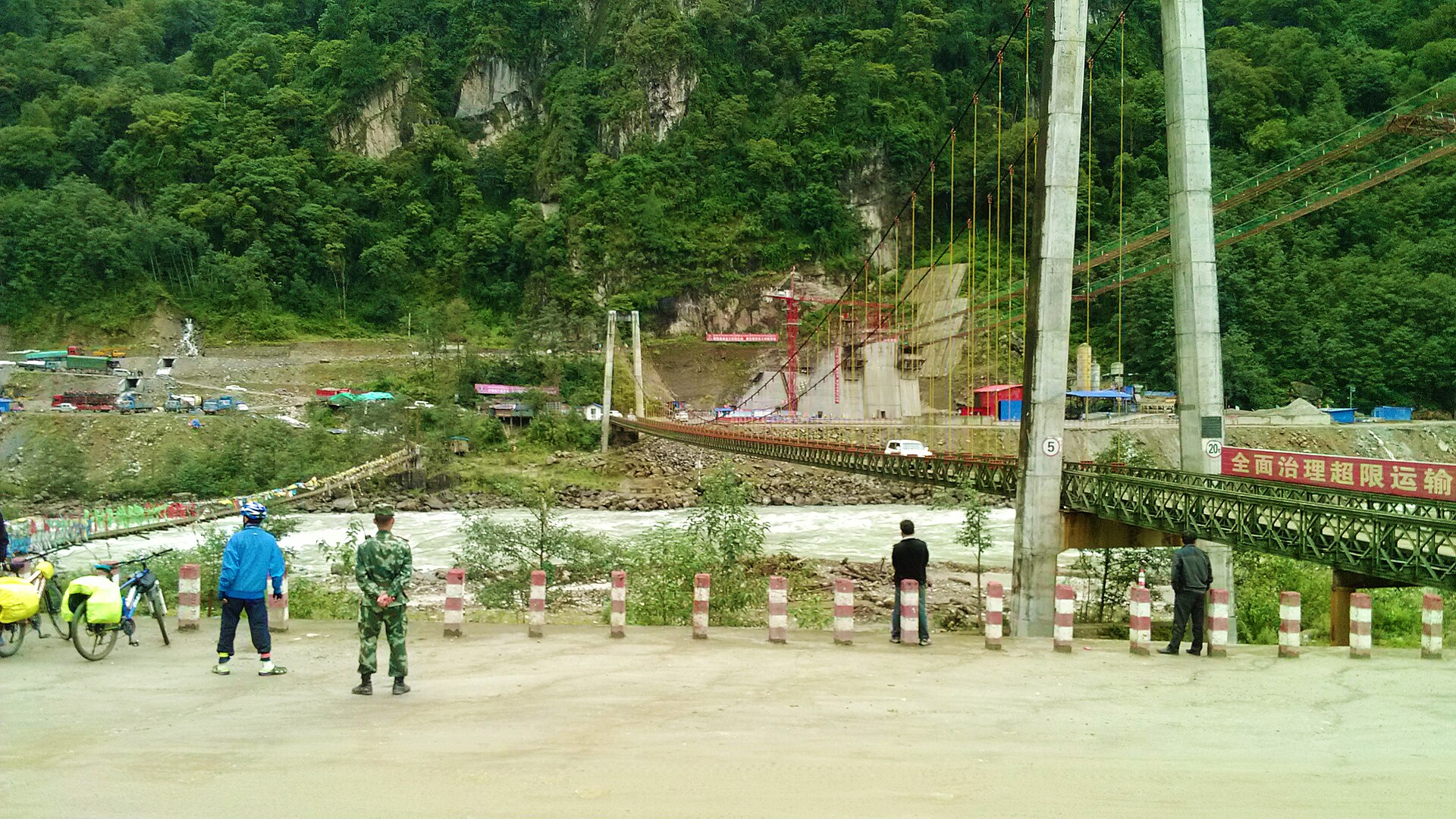 The Tongmai suspension bridge crosses a fast river beside road works in Bomi County, Tibet.