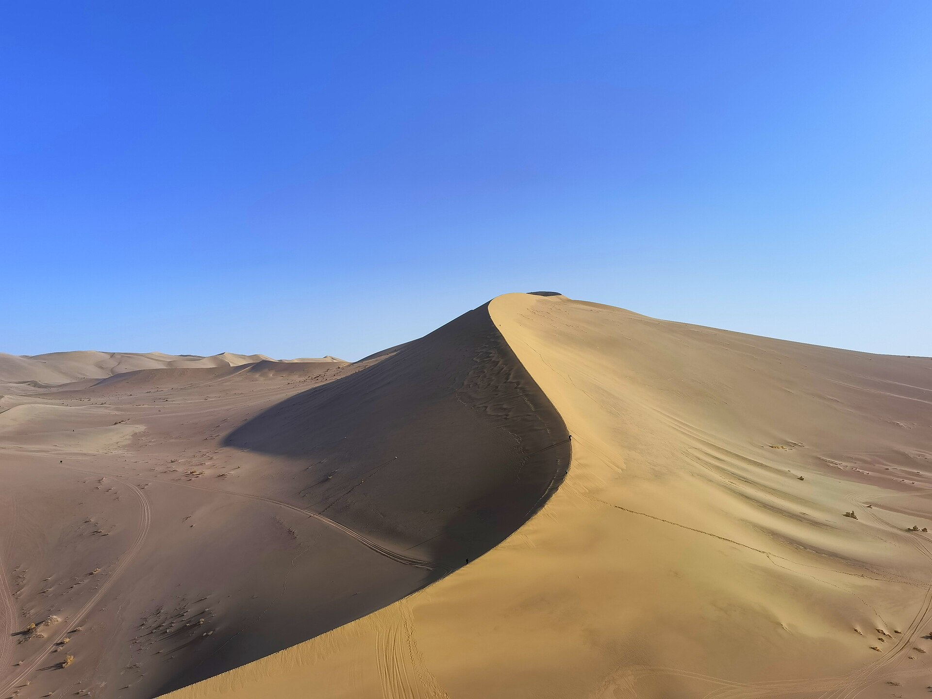 A sunlit sand ridge at Mingsha Mountain near Dunhuang under a clear blue sky in 2021.