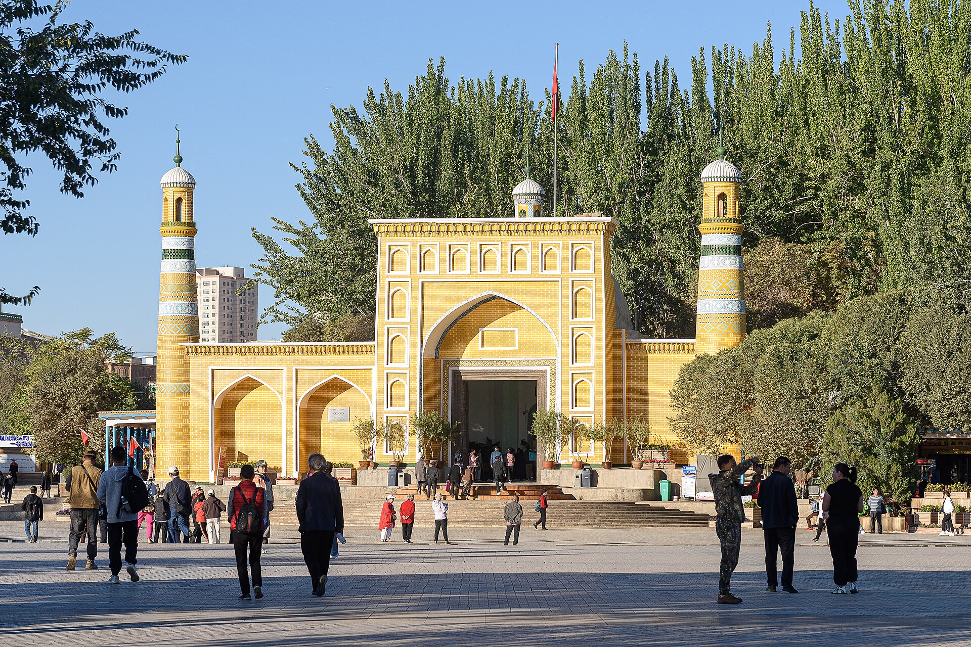 The yellow façade and two minarets of Id Kah Mosque face a public square with visitors in Kashgar.