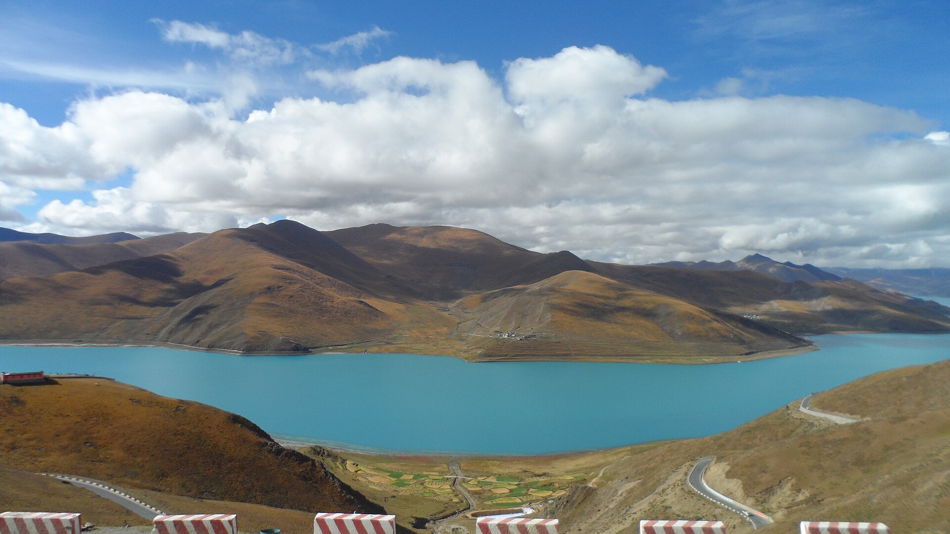 Yamdrok Lake, winding shoreline and surrounding brown hills seen from a roadside overlook in October 2019.