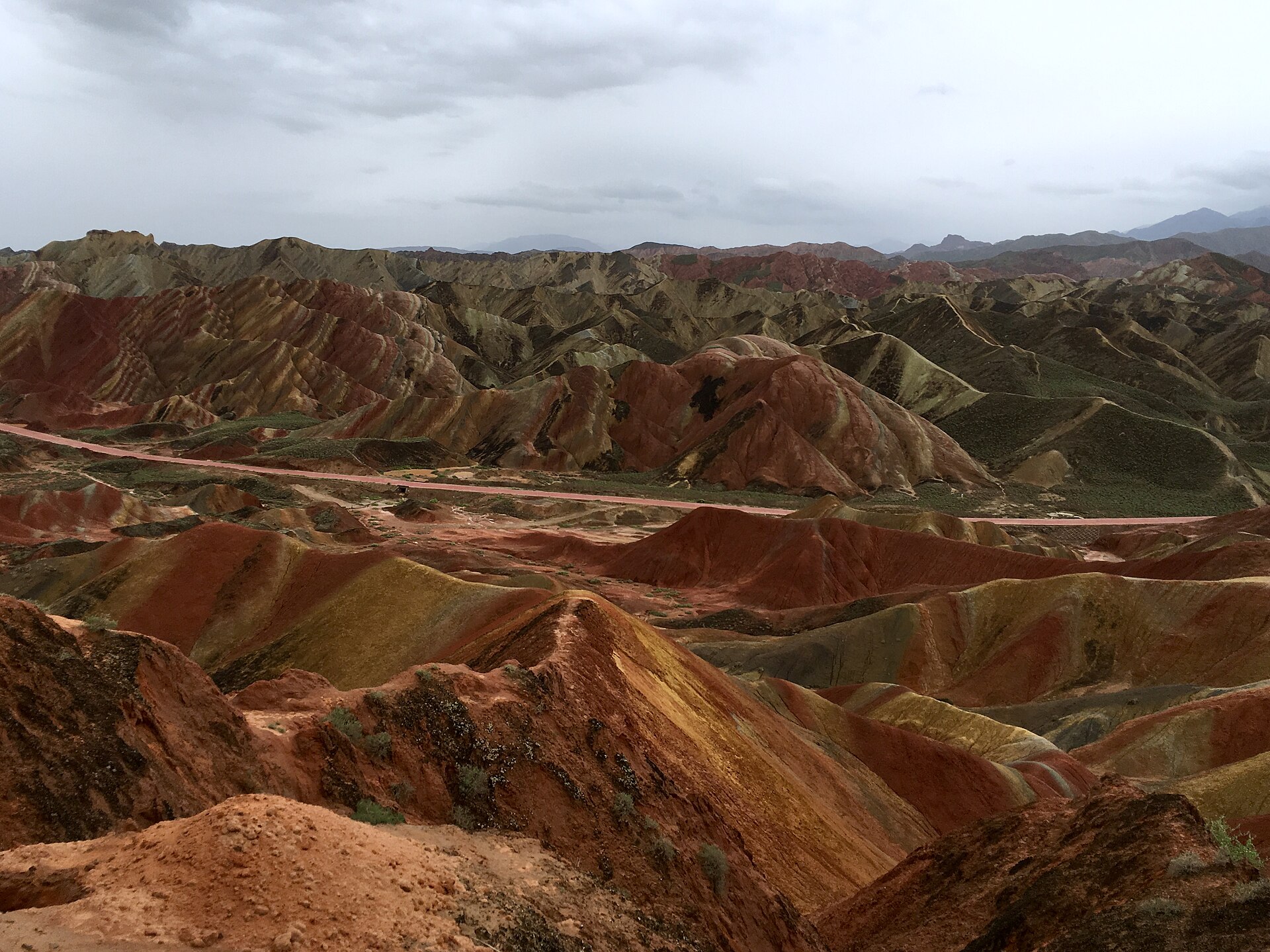 Dark red and green Danxia hills sit beneath a grey rain sky, with a road crossing the valley in Zhangye.